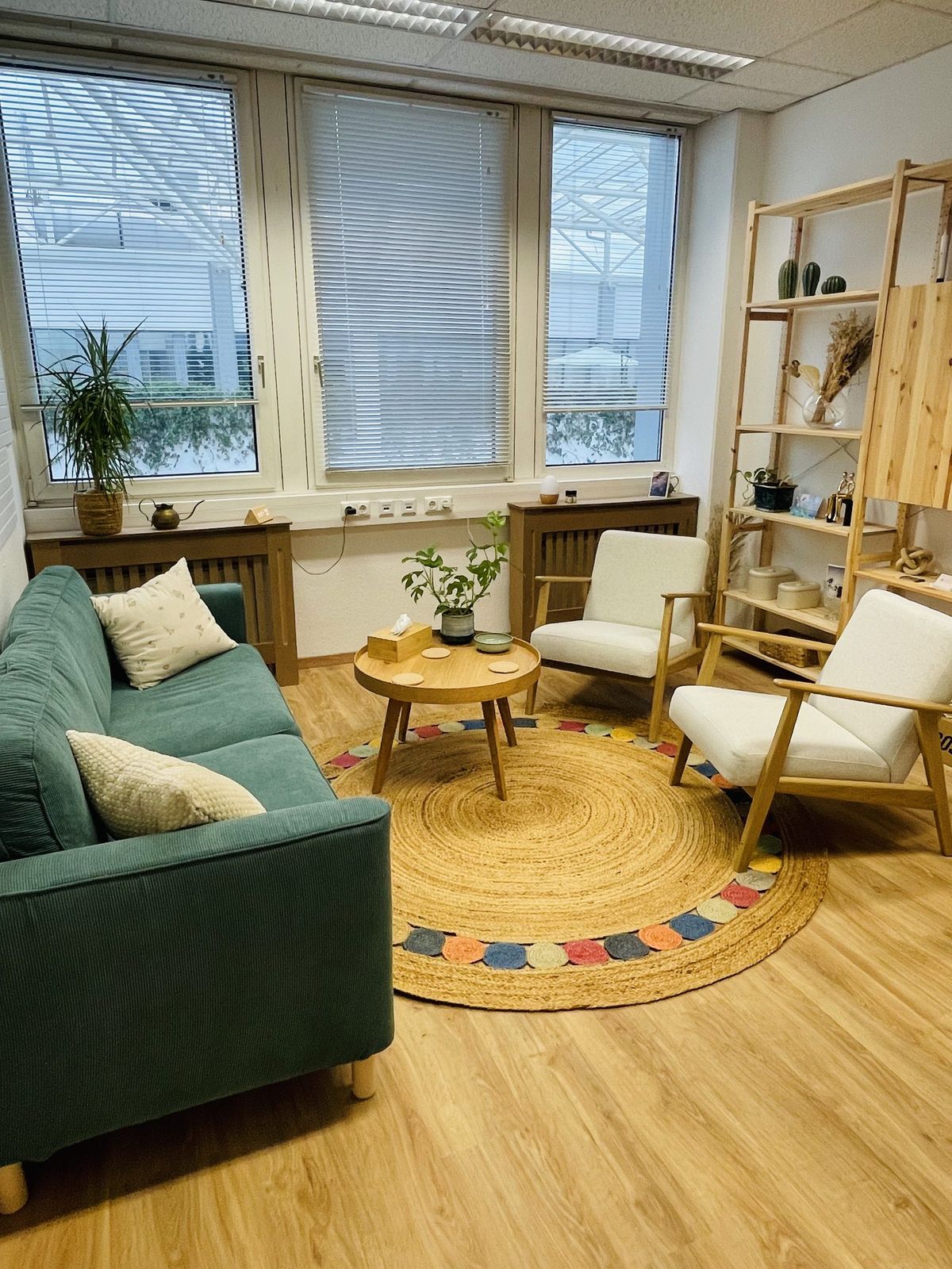 Praxisraum mit grünem Sofa, Sesseln und rundem Juteteppich